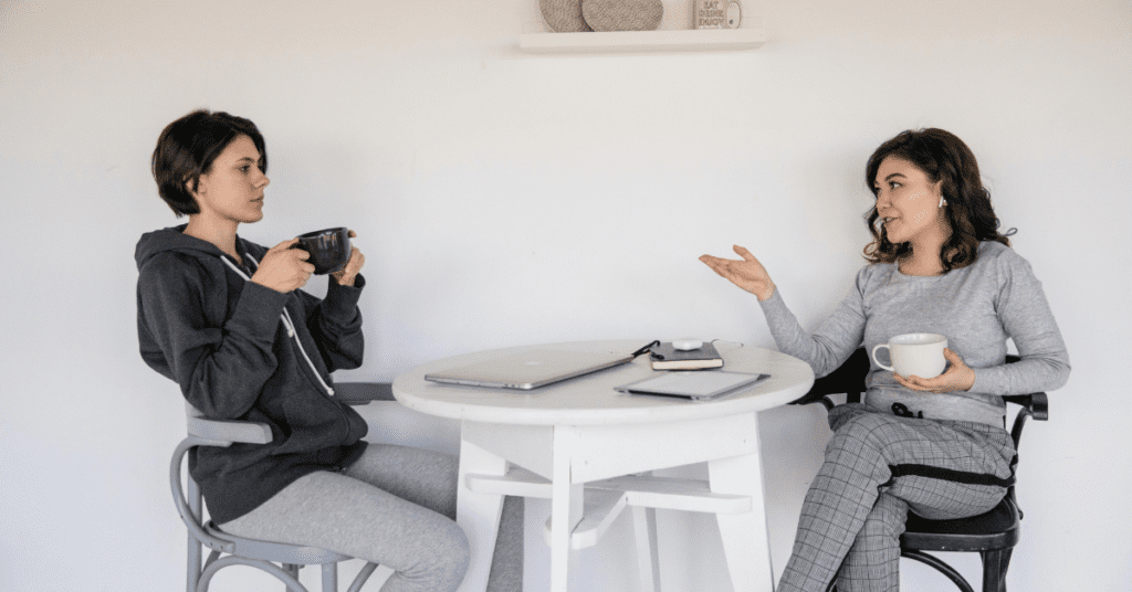 Two women talking at a table while drinking coffee.