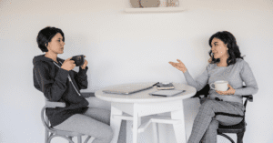 Two women talking at a table while drinking coffee.