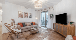 A boho style living room that has a couch with pillows, a wicker cabinet and TV, an armchair, and a chandelier.