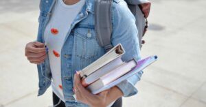 college student holding a stack of books and folders in arms