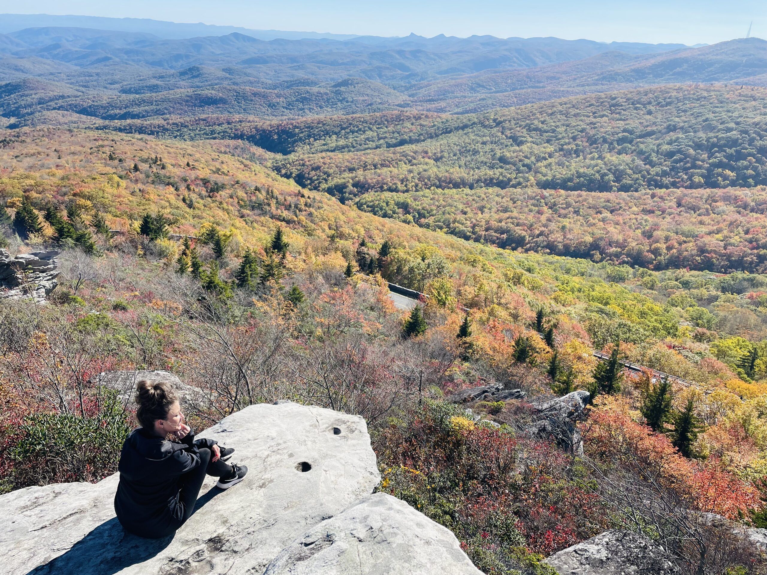 Woman sitting on a rock overlooking trees with fall colors after a hike.