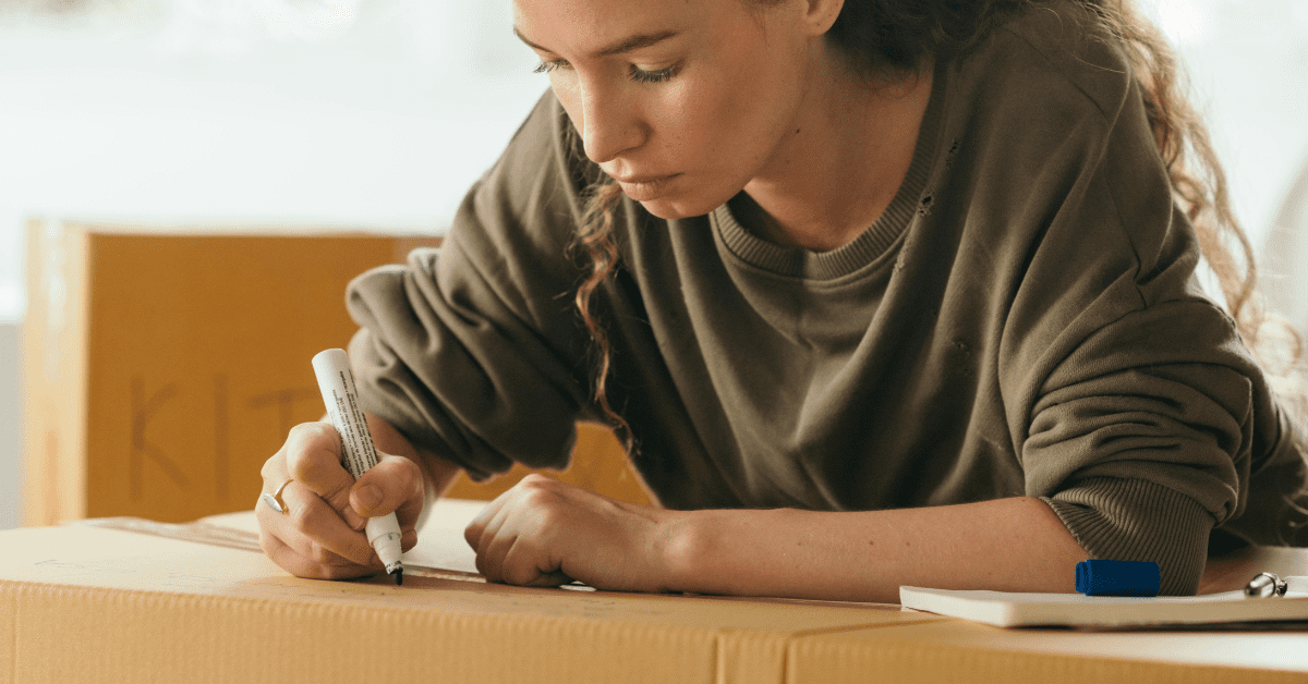 Image of a woman writing on a cardboard box, preparing to move to a new house.