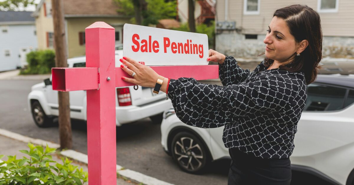 Image of a Realtor hanging a "Sale pending" sign