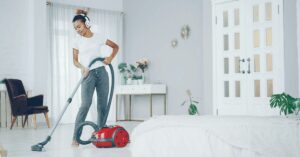 A woman vacuuming her house that has white walls and a white couch
