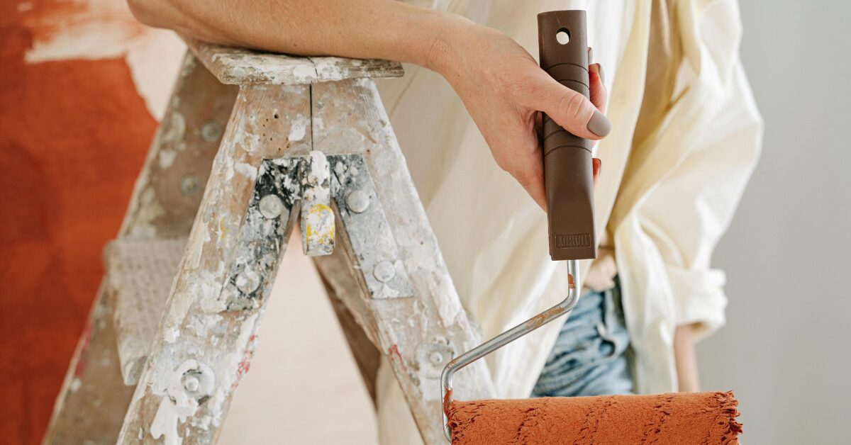 Someone holding a paint roller and standing on a ladder