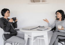 Two women talking at a table while drinking coffee.