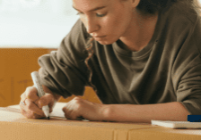 Image of a woman writing on a cardboard box, preparing to move to a new house.