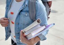 college student holding a stack of books and folders in arms